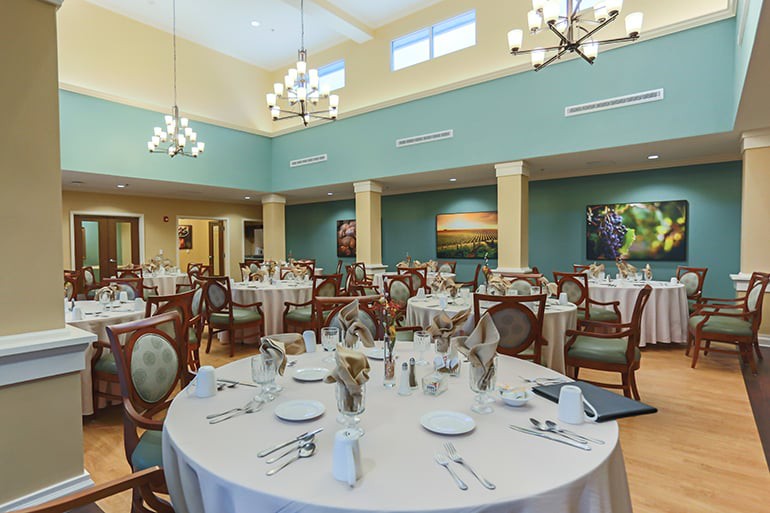 An elegant dining room with neatly arranged tables and chairs, featuring chandeliers and tasteful decor.