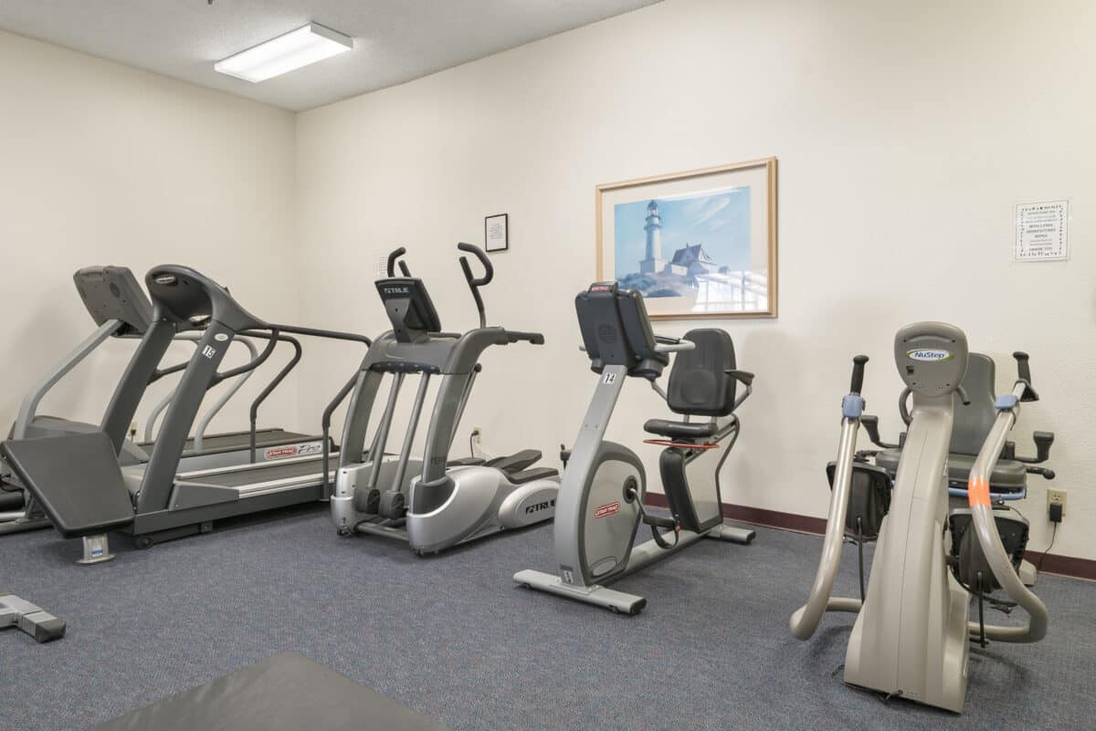 A small gym with various exercise machines including treadmills, ellipticals, and a stationary bike.