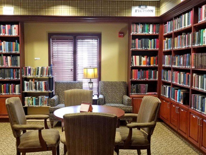 A cozy library reading area with bookshelves, chairs, and a table under warm lighting.