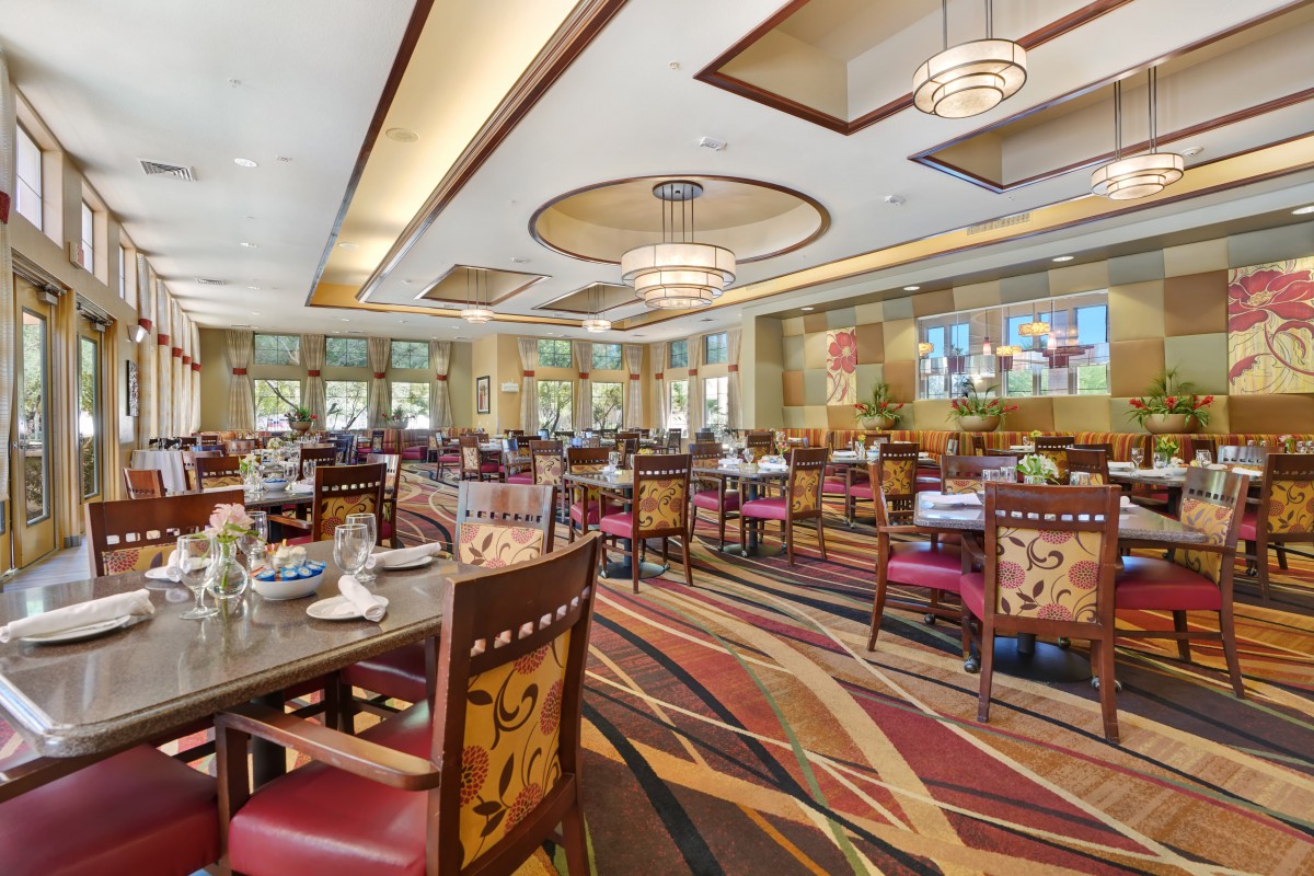 A spacious and elegantly designed restaurant dining area featuring stylish chandeliers, patterned carpets, and neatly arranged tables and chairs.