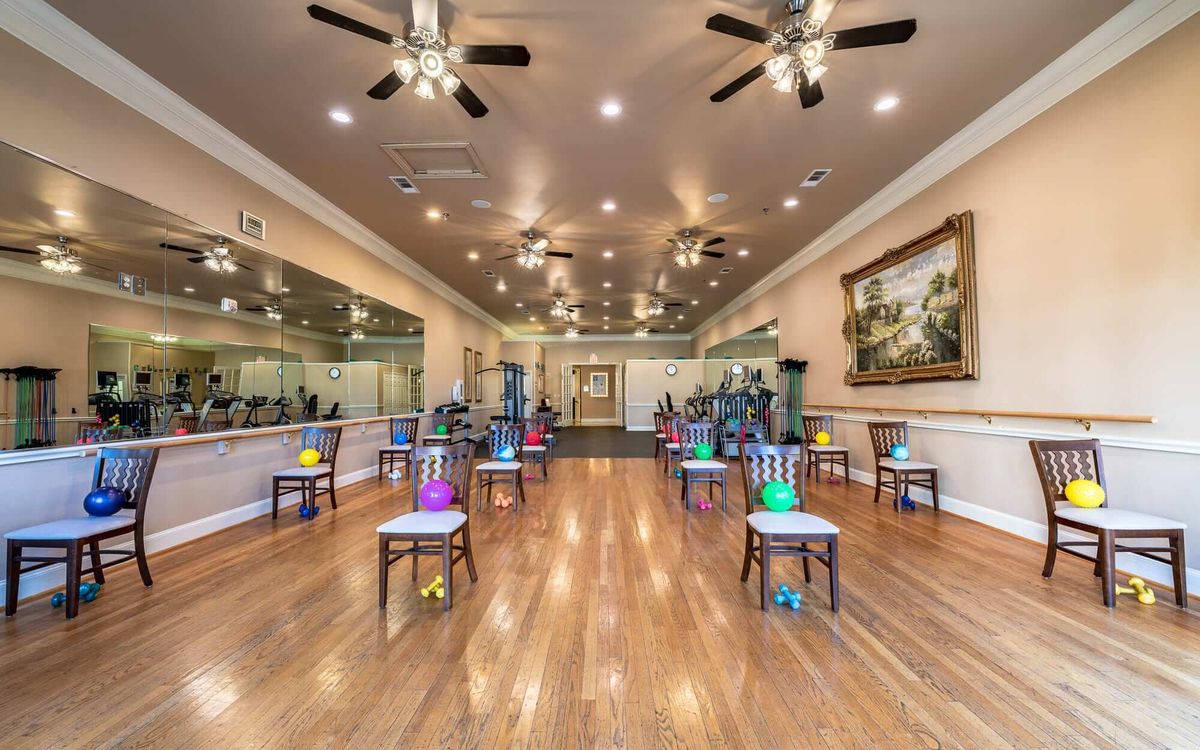 An exercise room with chairs arranged in rows, each equipped with a colorful exercise ball on top, reflective mirrors on the walls, and ceiling fans providing ventilation.