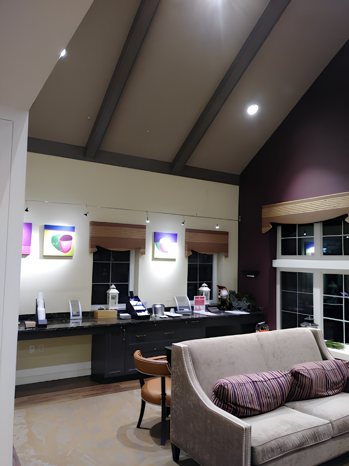 A cozy living room with a vaulted ceiling, showcasing artwork, a comfortable sofa, and a desk by the window.