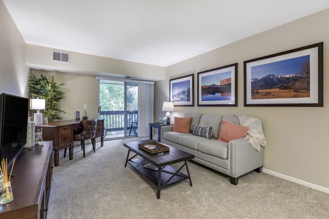A cozy living room with a sofa, coffee table, and dining area, decorated with wall art.