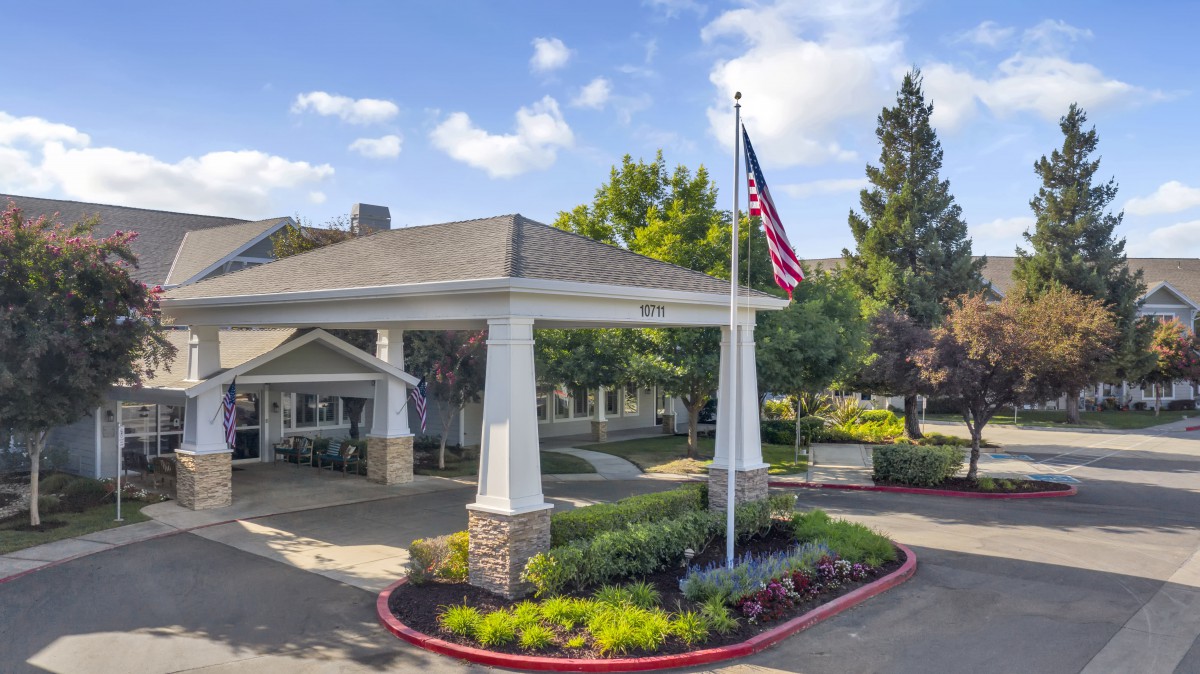 An entrance area with a flagpole and landscaped surroundings on a sunny day.