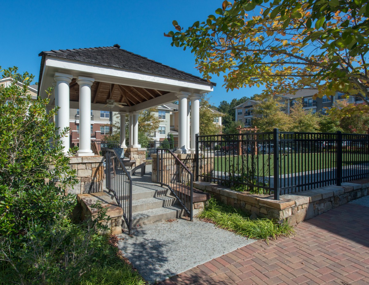 A charming gazebo surrounded by greenery under a clear blue sky.