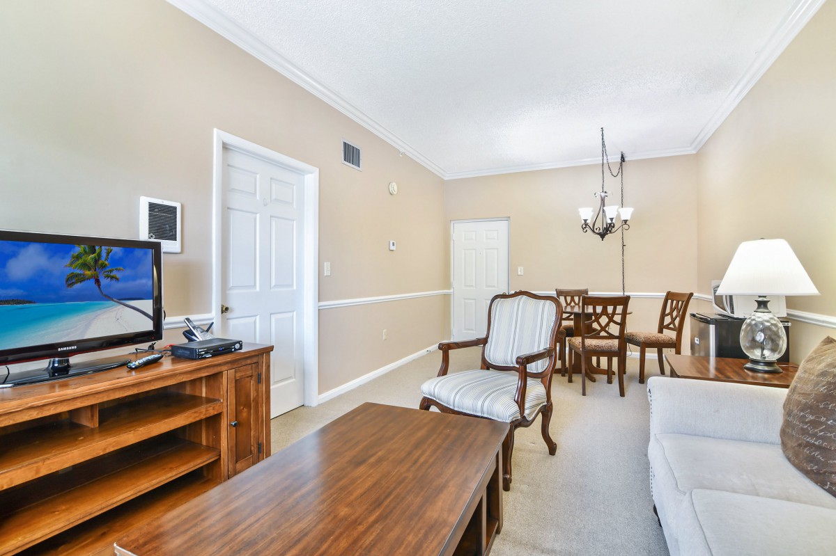 A cozy living room with a television, wooden furniture, and a dining area featuring a chandelier.