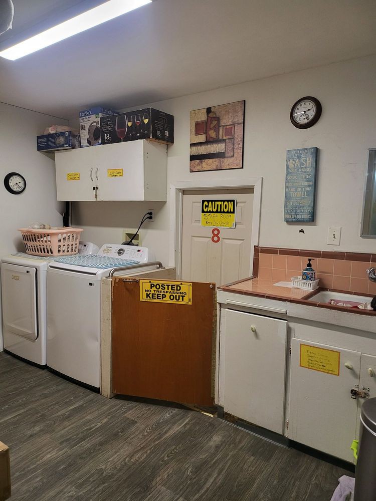 A laundry room featuring a washing machine, dryer, sink, and storage cabinets with various decorations on the walls.
