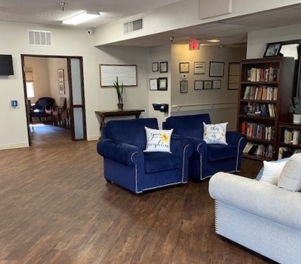 A cozy living room featuring blue and white couches, a bookshelf, and warm wooden flooring.