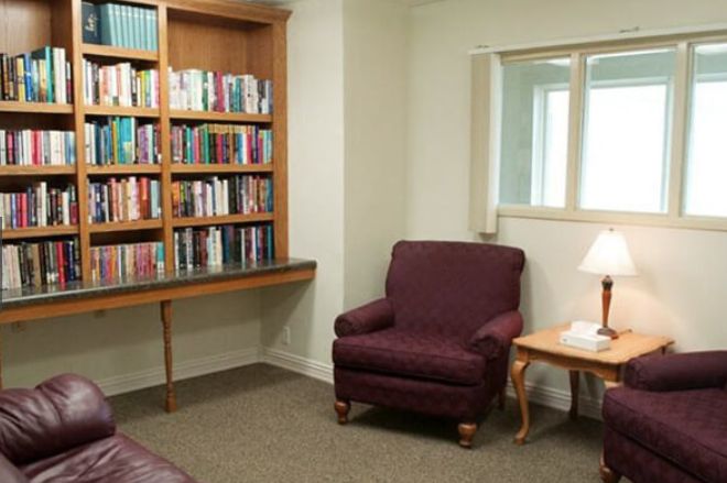 A cozy reading nook featuring a bookshelf and an armchair with a lamp.