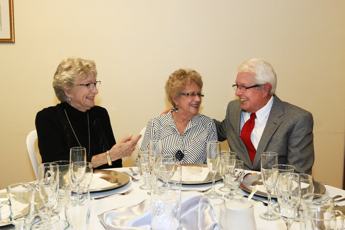 A group of three elderly individuals enjoying a conversation at a dinner event.
