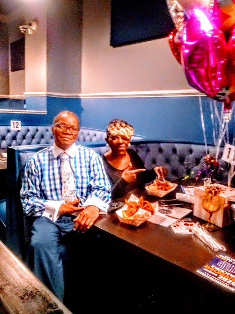A couple enjoying a meal at a restaurant, celebrating with balloons and gifts on the table.