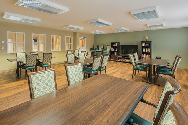 A spacious dining room with multiple tables and chairs, featuring a wooden floor and a television in the background.