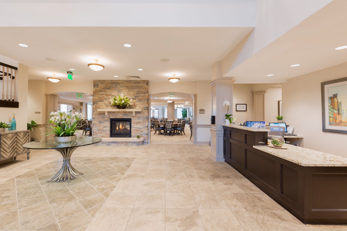 A spacious and well-decorated lobby featuring a central fireplace, tiled flooring, and a reception desk.
