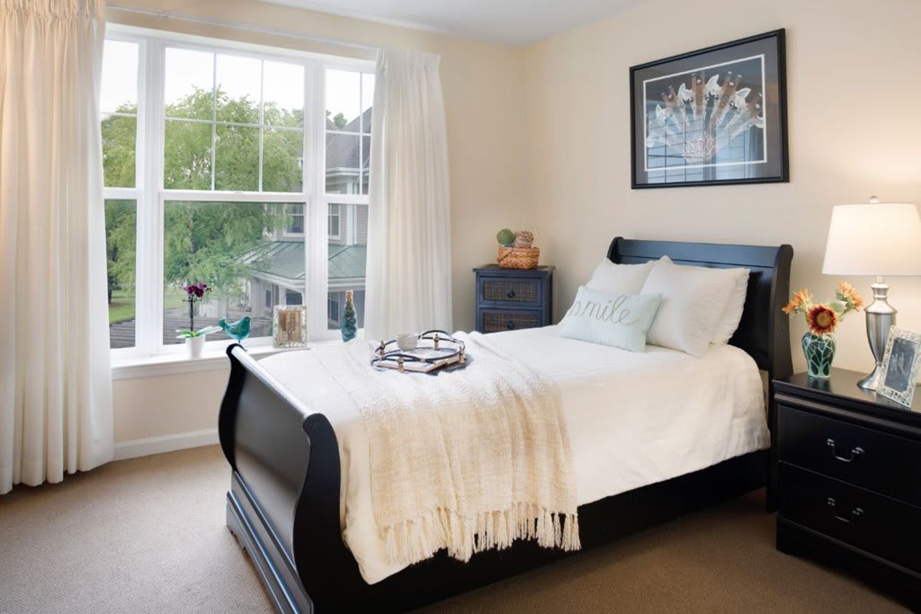 A cozy bedroom with a sleek black bedframe, white bedding, and a large window offering natural light.
