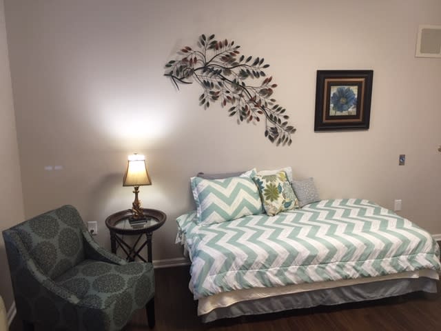 A cozy bedroom features a bed with chevron-patterned bedding, accompanied by a decorative wall piece and a lamp on a side table.