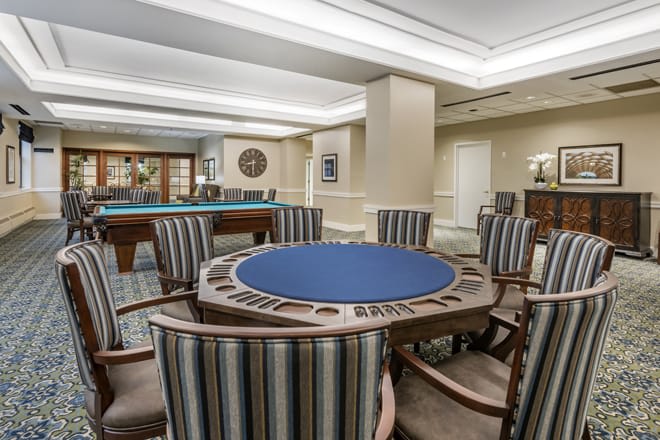 A stylish game room featuring a poker table and a pool table, with comfortable seating and elegant interior design.