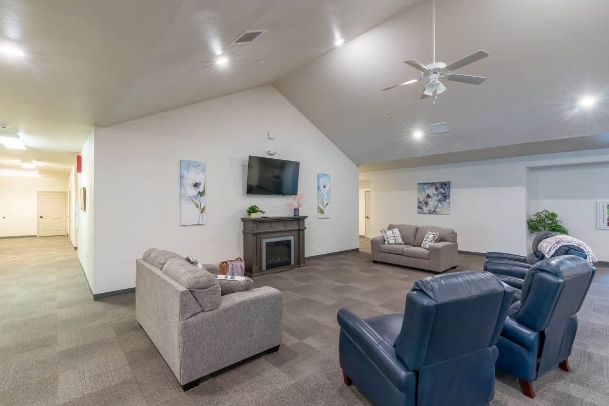 A spacious living room featuring comfortable sofas and armchairs, a television mounted above a fireplace, and a ceiling fan overhead.