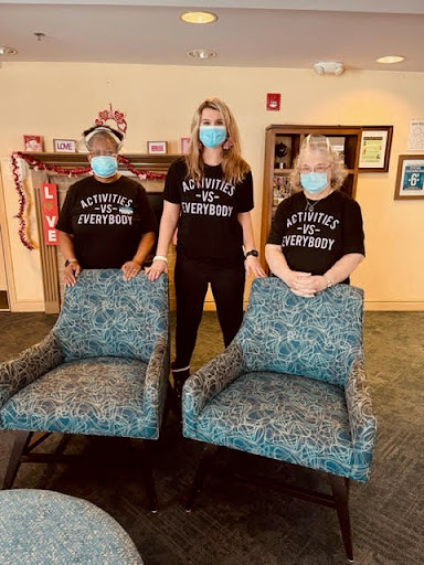 A group of individuals wearing masks stands next to two chairs, promoting safety during a community gathering.