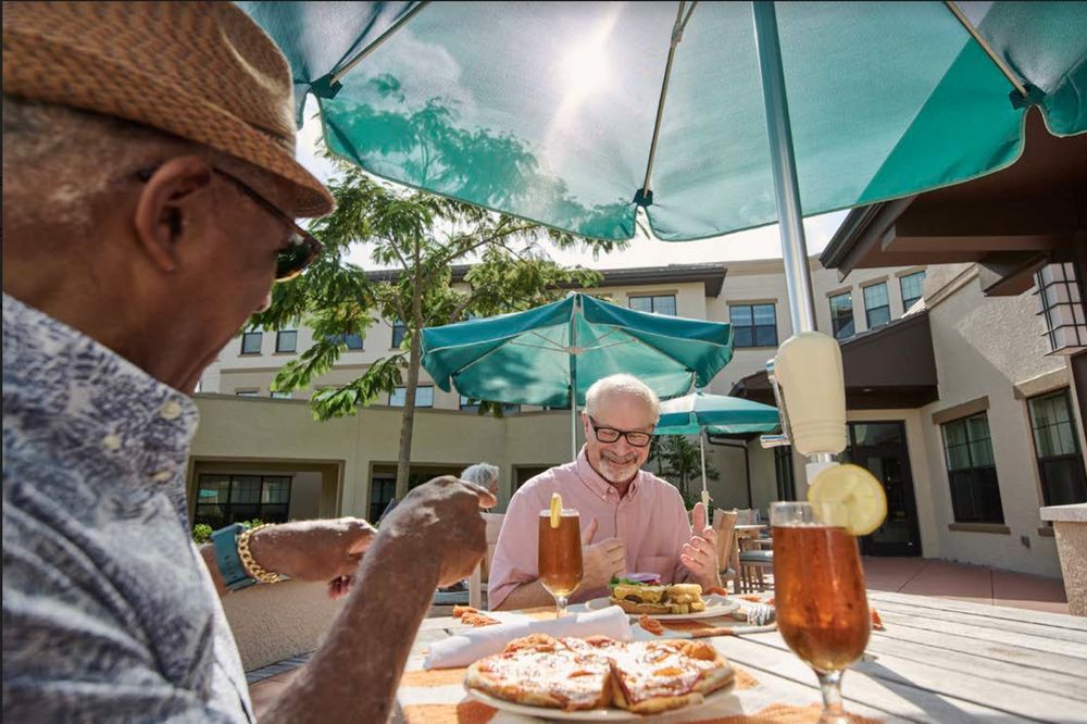 Elderly friends enjoying a sunny meal outdoors under umbrellas.
