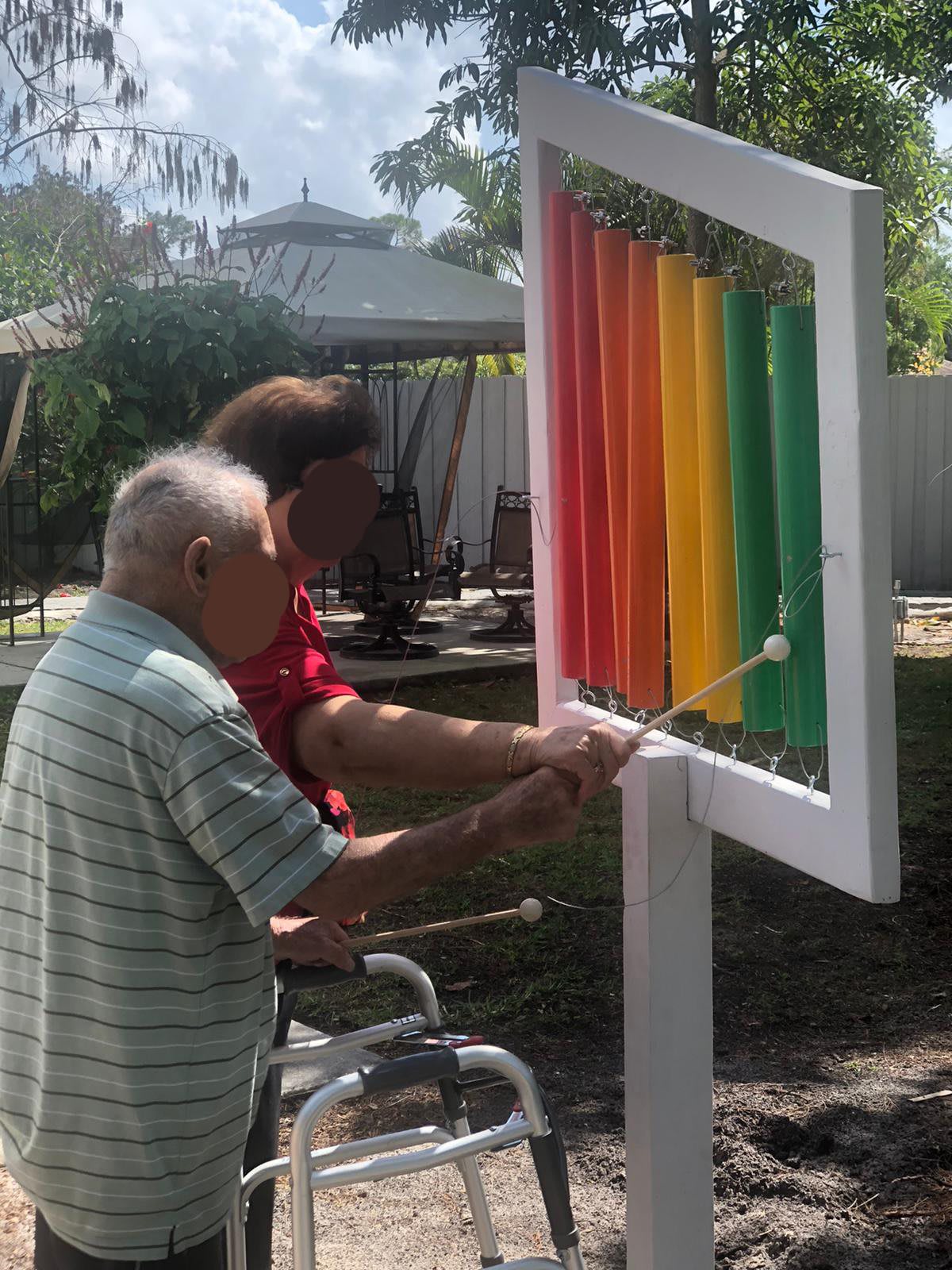 Two people playing a colorful outdoor xylophone in a garden setting.