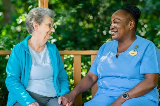 A nurse and an elderly woman share a moment of companionship outdoors.