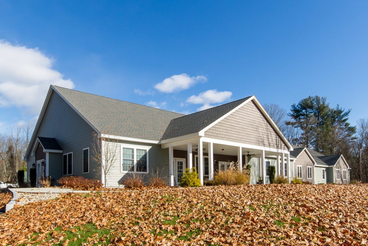 A suburban house with autumn leaves covering the front yard under a blue sky.