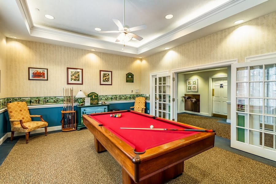 A cozy recreation room featuring a pool table with red felt, decorated with wall art and illuminated by a ceiling fan.