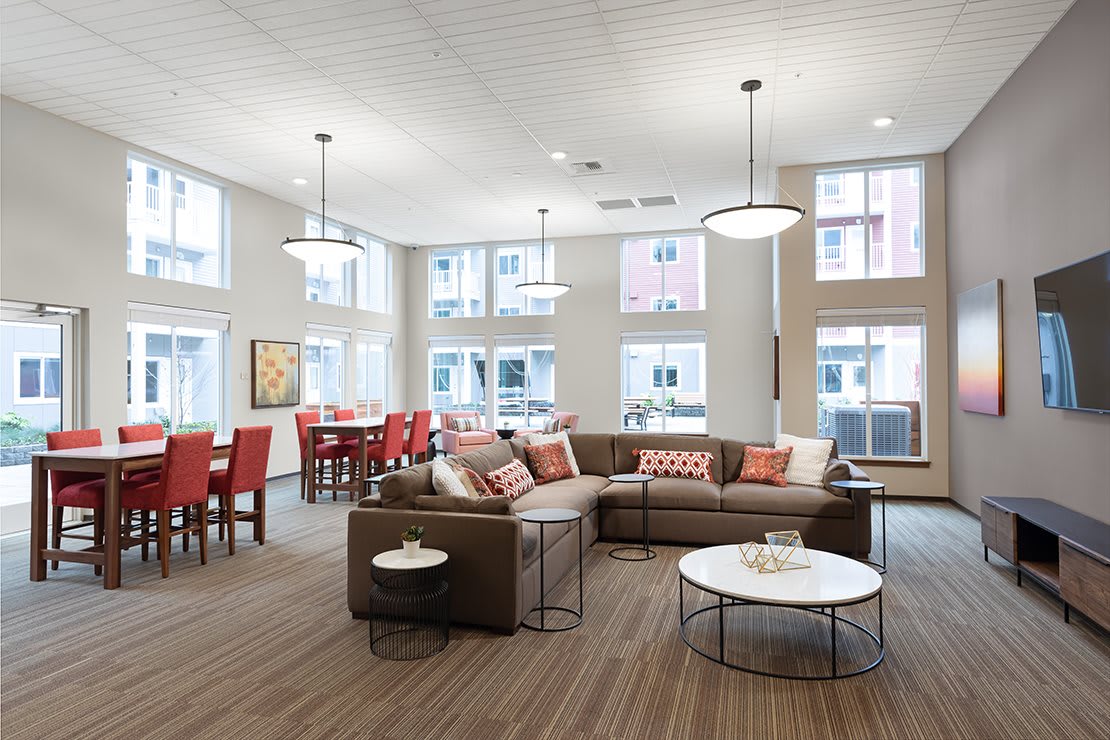 A spacious and modern living room with a sectional sofa, coffee table, and dining area under large windows.