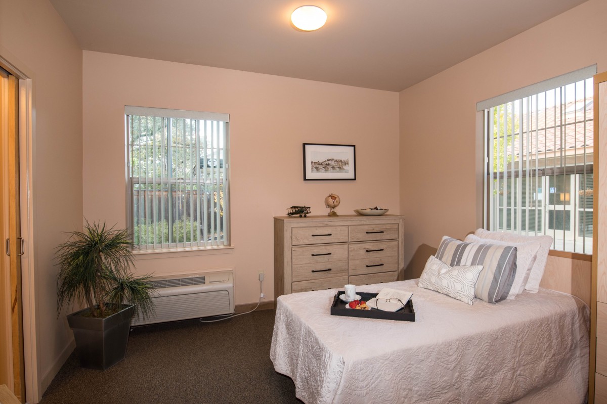 A cozy bedroom with a neatly made bed, dresser, and natural light from the windows.