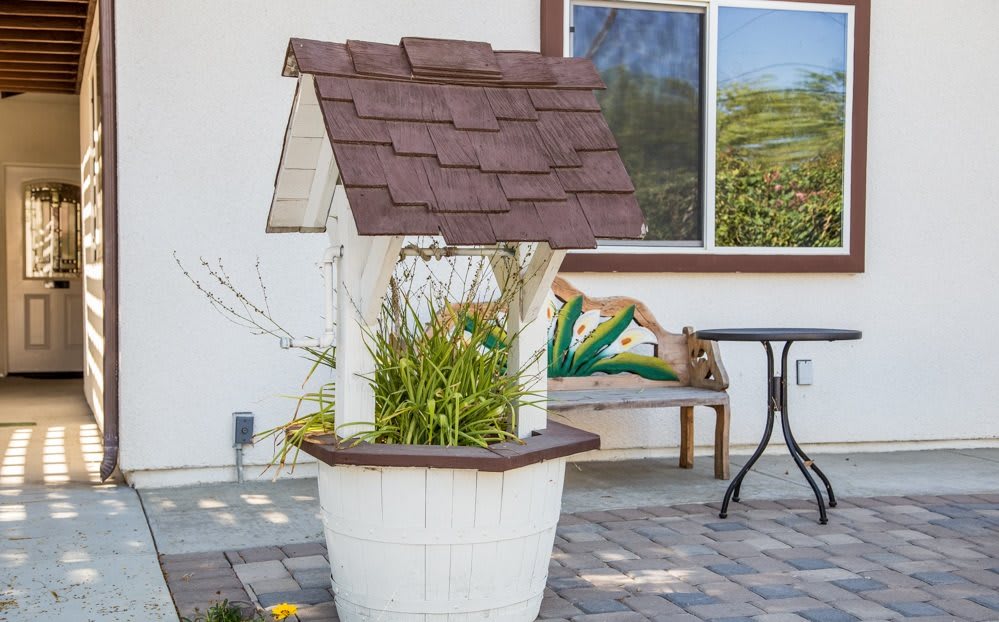 A decorative wishing well with plants in a patio setting next to a bench.