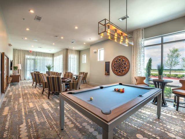 A modern game room featuring a pool table and dartboard, with seating areas and contemporary lighting.