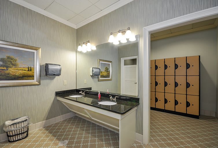 A well-lit bathroom with dual sinks and mirrors, adjacent to a locker area.