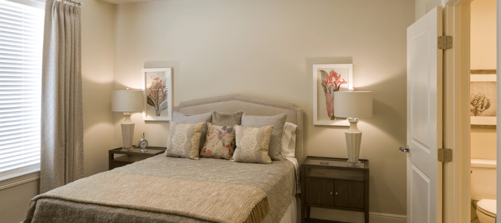 A cozy and well-decorated bedroom with a neatly made bed flanked by nightstands and lamps, adorned with framed artwork on the walls.