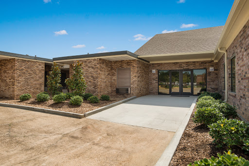 A welcoming entrance to a well-maintained commercial building with lush landscaping and a clear blue sky.