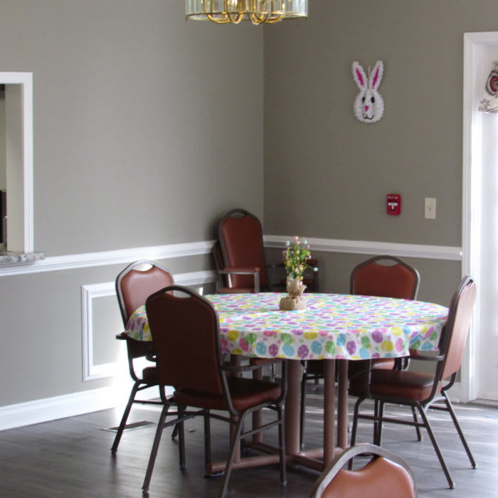 A cozy dining area with a round table, surrounded by chairs and adorned with a decorative wall hanging in the background.