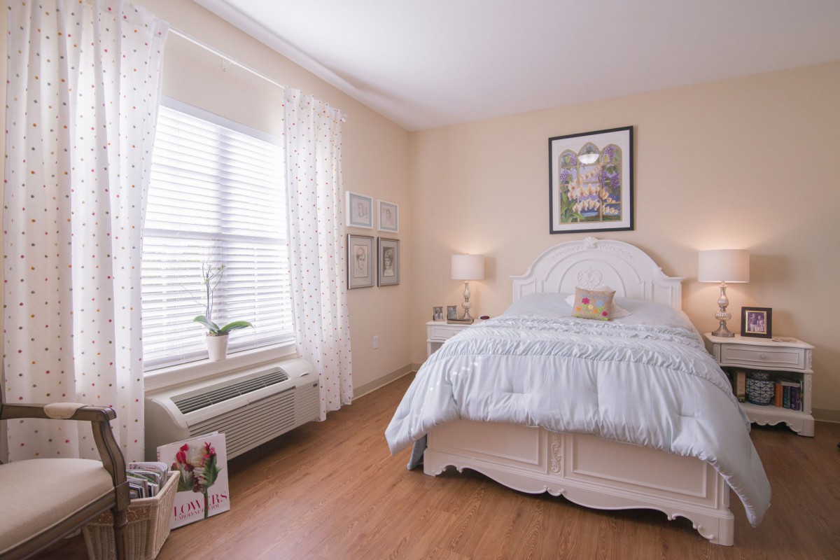 A cozy bedroom with a neatly made bed, artwork on the wall, and natural light streaming through the window.