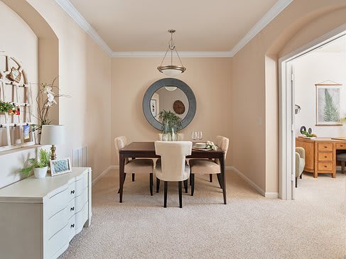 A stylish dining room with a large mirror, elegant table, and cushioned chairs.