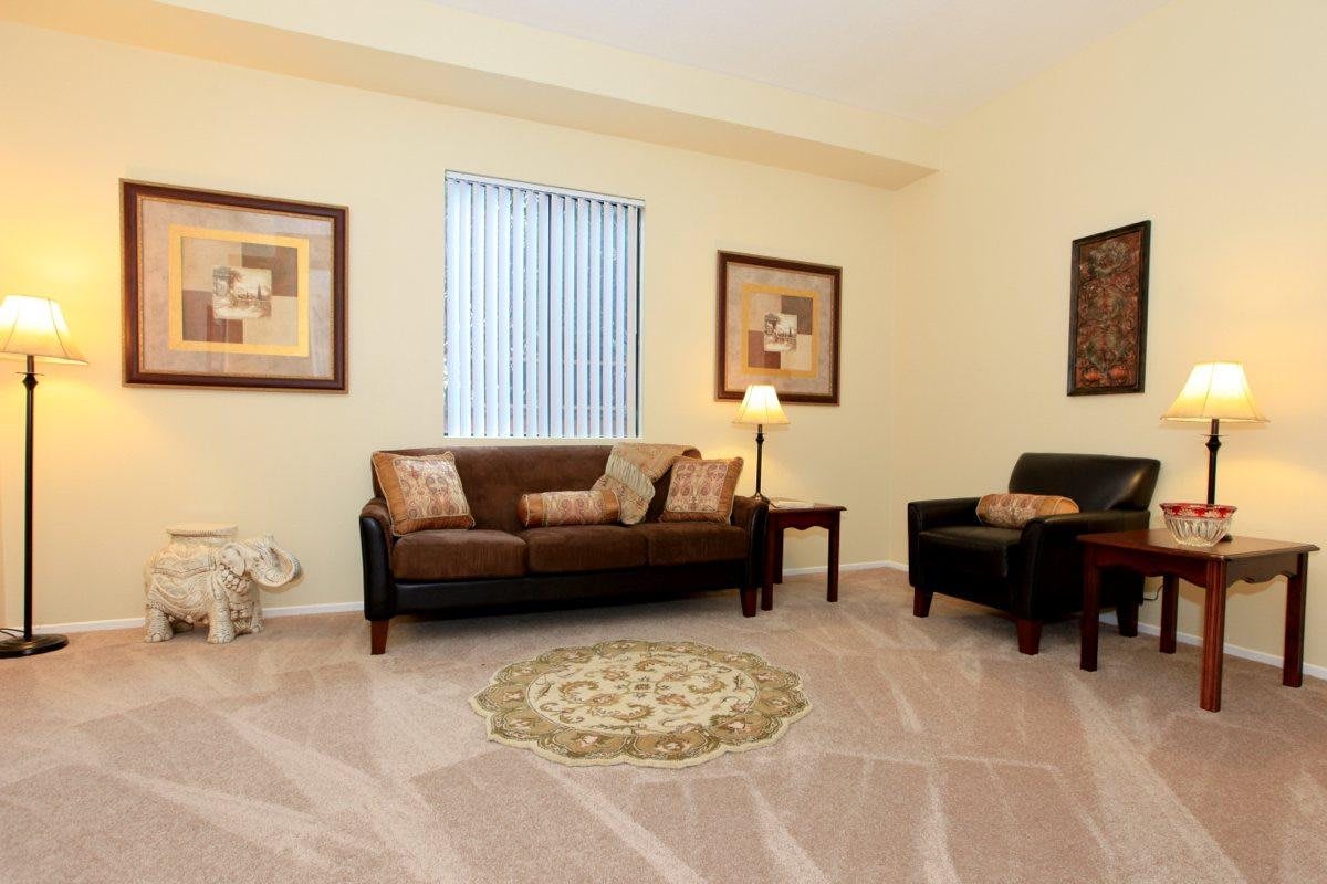 A cozy living room with a brown sofa, armchair, and decorative pillows, complemented by wall art and a central rug.