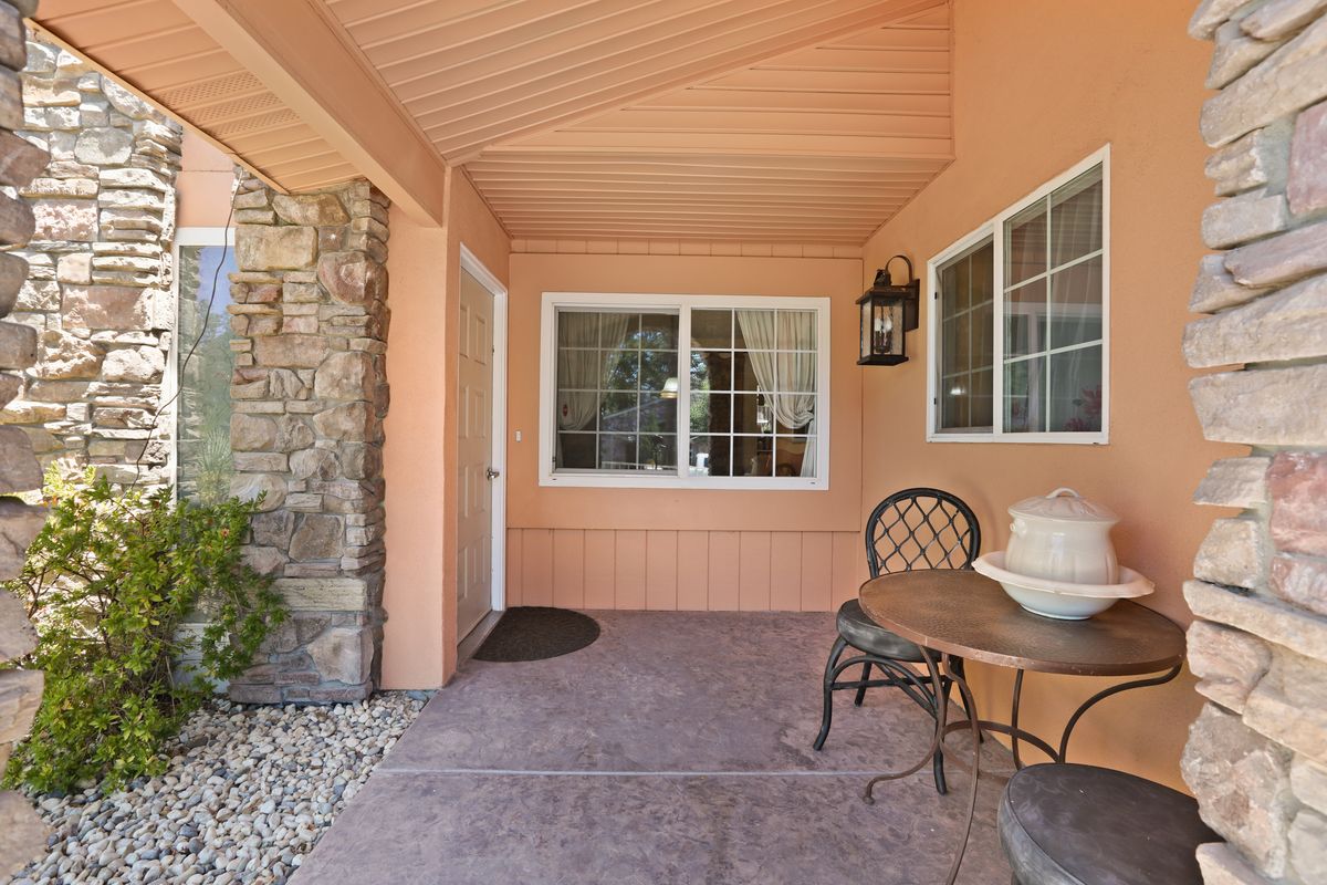 A cozy porch area with a table and two chairs, featuring a stone wall and windows.
