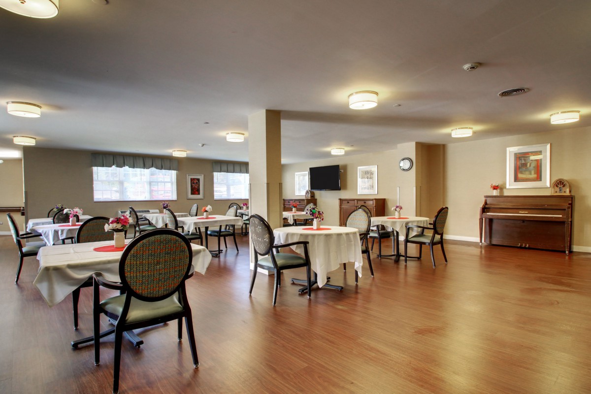 A spacious dining area with multiple tables and chairs, featuring soft lighting and wooden flooring.