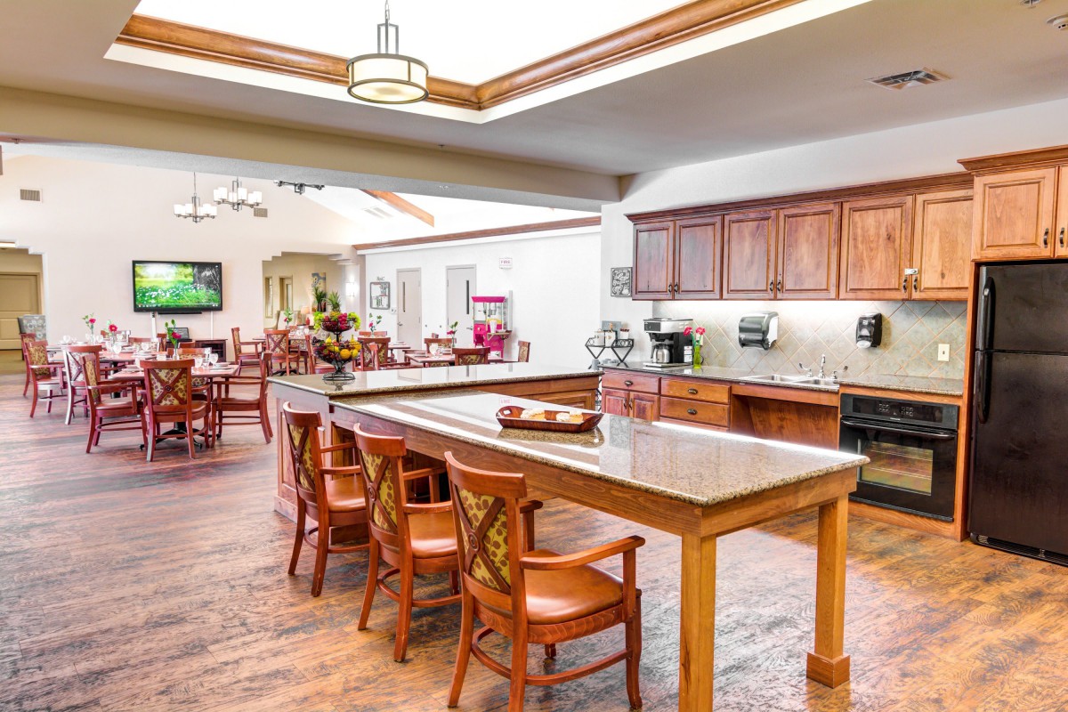 A spacious kitchen and dining area featuring a long wooden table with chairs, wooden cabinets, and bright overhead lighting.