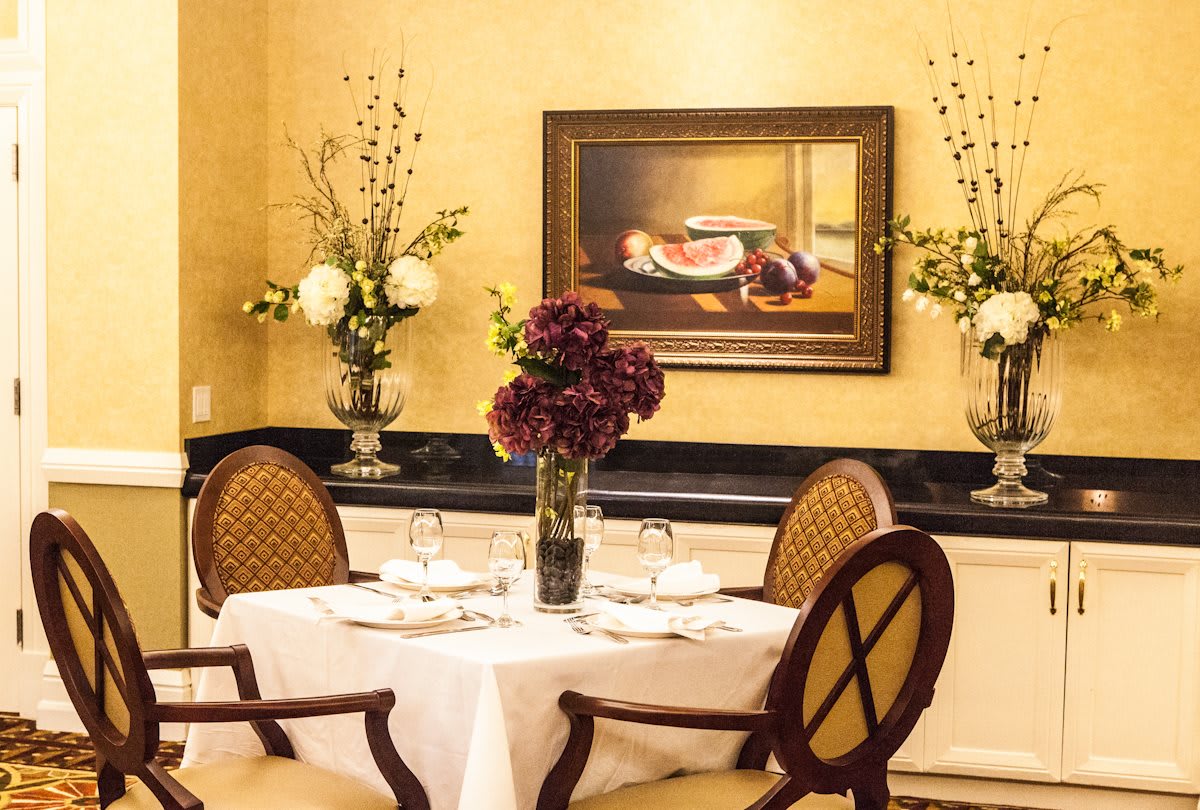 An elegantly set dining table with a floral centerpiece and framed painting in the background.