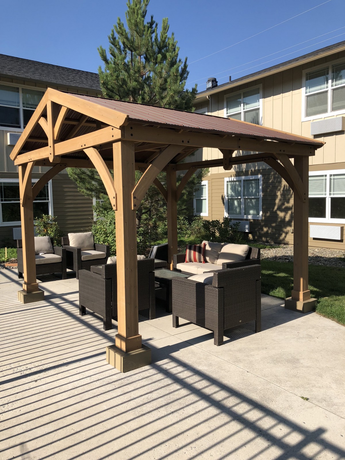 A wooden pergola with comfortable patio furniture set in a sunny backyard.