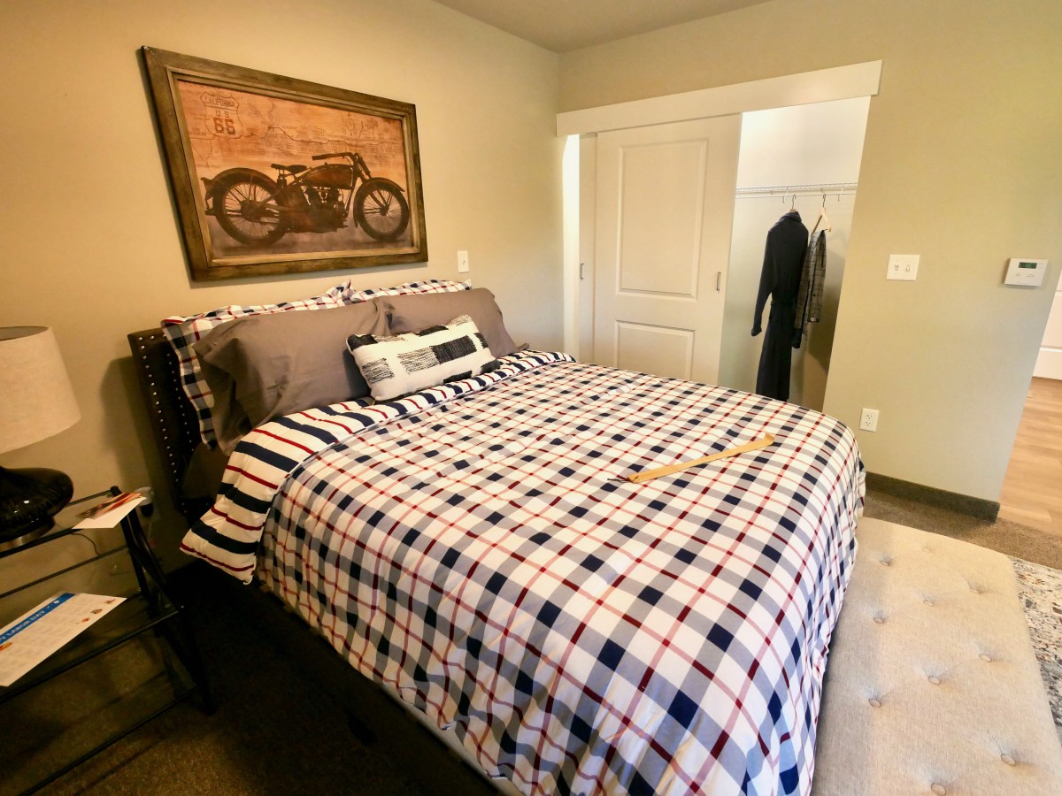 A cozy bedroom featuring a bed with plaid bedding and a motorbike picture on the wall.