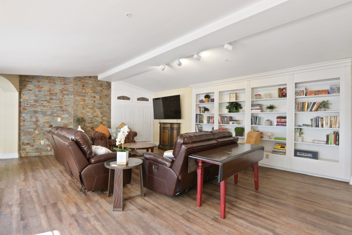 A modern living room featuring comfortable leather sofas, built-in bookshelves, and a large television, all set on elegant wooden flooring.