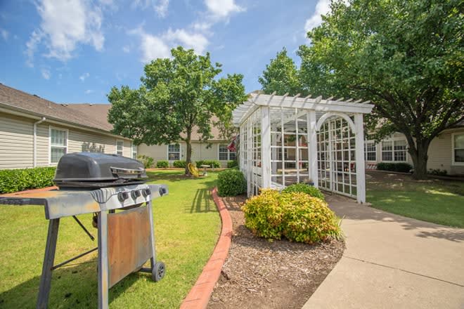 A beautifully landscaped garden with a pergola and grill set in a sunny outdoor setting.