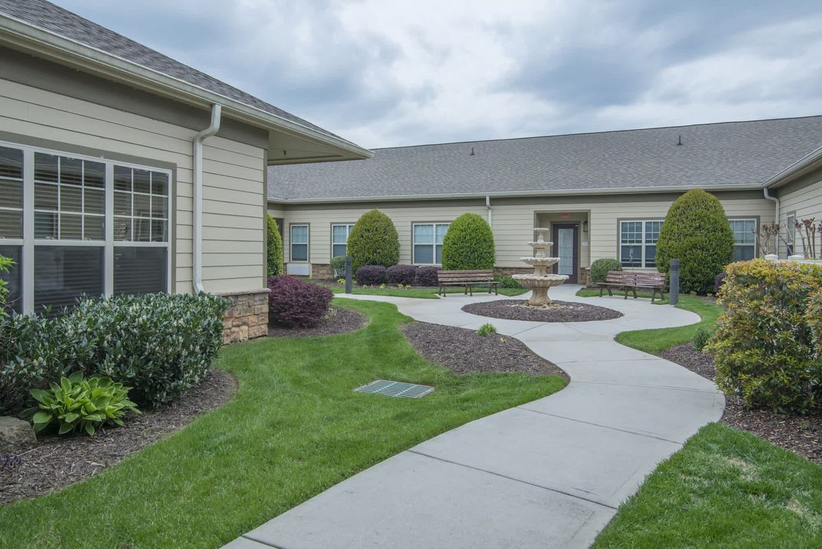 A well-maintained courtyard with a walkway winding through neatly landscaped shrubs and grass, surrounded by buildings under an overcast sky.