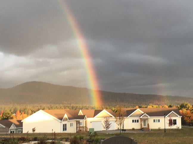 A vibrant rainbow arcs over a cluster of houses against a cloudy sky.
