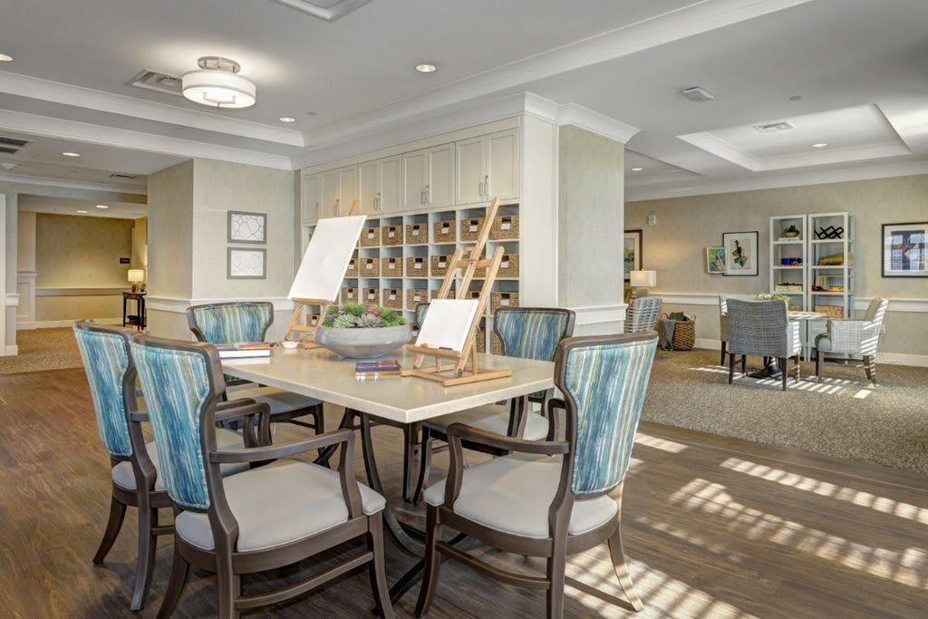 A cozy interior dining area with art supplies and easels on a table, illuminated by natural light.
