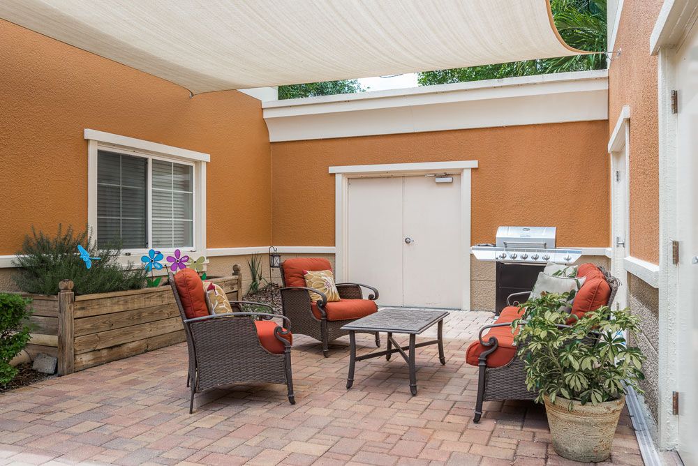 A cozy patio with rattan seating, a central table, and a grill under a shaded canopy.